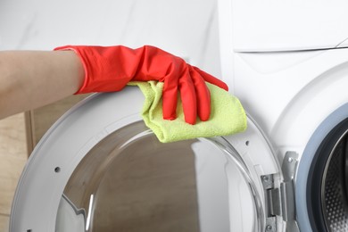 Photo of Woman cleaning washing machine with rag indoors, closeup