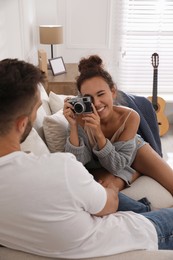 Beautiful African-American woman taking picture of her boyfriend on sofa at home