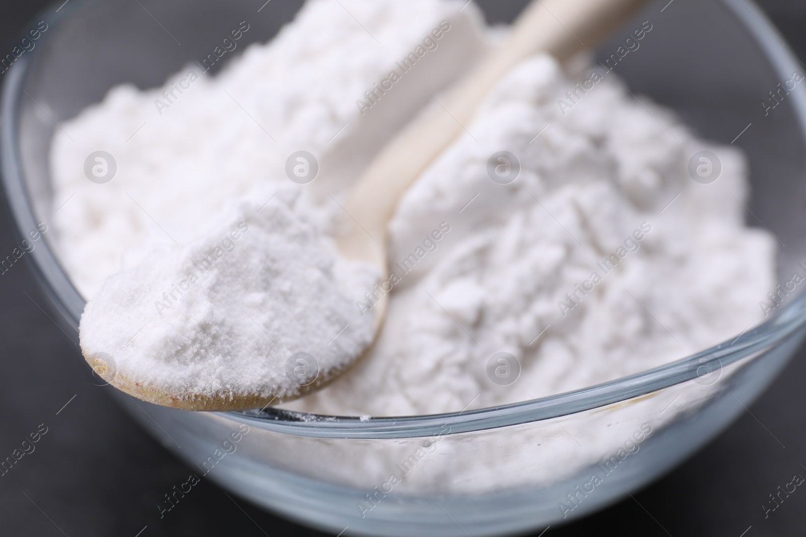 Photo of Glass bowl and wooden spoon of natural starch on black table, closeup