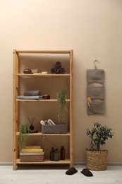 Photo of Shelving unit with soft towels, plants and bottles indoors