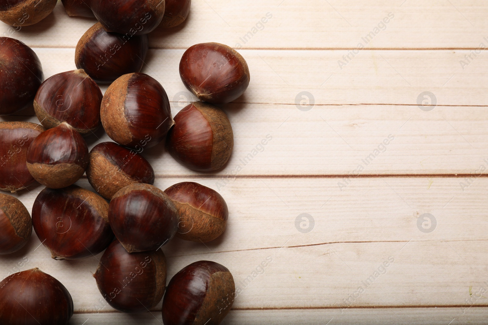 Photo of Sweet fresh edible chestnuts on light wooden table, top view. Space for text