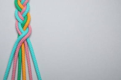 Photo of Top view of braided colorful ropes on light grey background, space for text. Unity concept