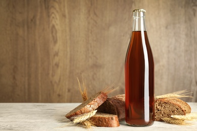 Bottle of delicious fresh kvass, spikelets and bread on white wooden table. Space for text