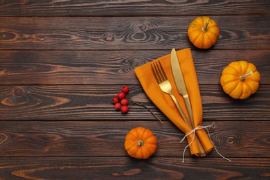 Photo of Cutlery, napkin and pumpkins on wooden background, flat lay with space for text. Table setting