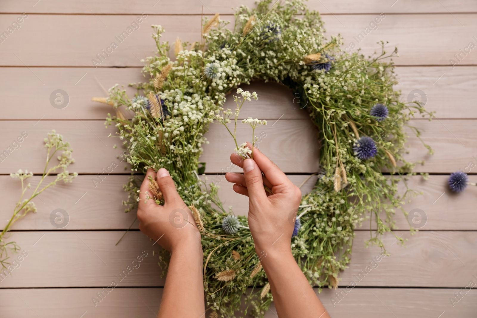 Photo of Woman making beautiful wreath of wildflowers at wooden table, top view
