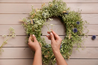 Woman making beautiful wreath of wildflowers at wooden table, top view