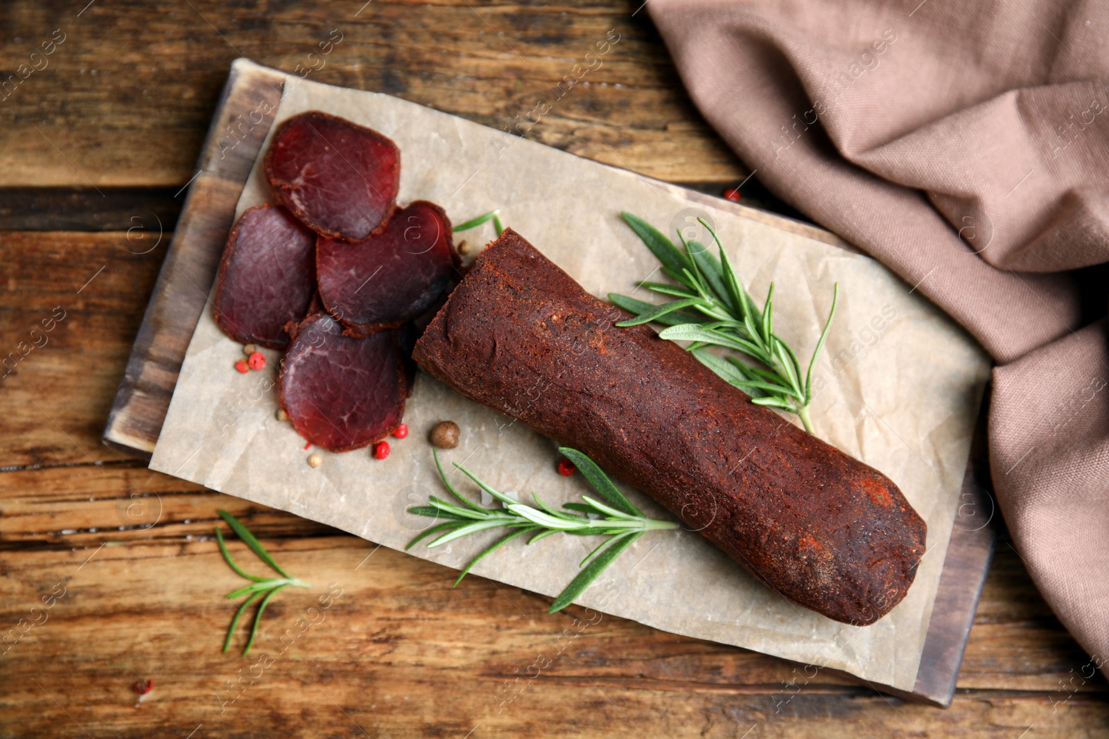 Photo of Delicious dry-cured beef basturma with rosemary and peppercorns on wooden table, flat lay