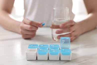 Woman with pills, organizer and glass of water at white marble table, selective focus