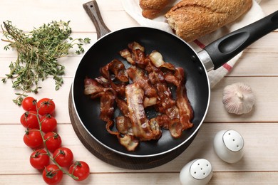 Photo of Delicious bacon slices in frying pan and products on light wooden table, flat lay