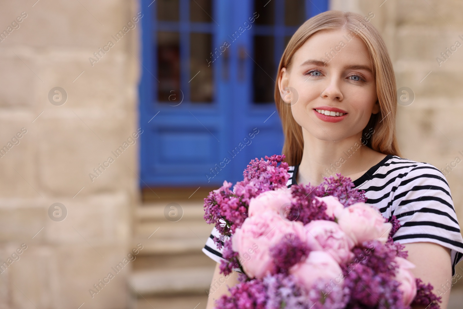 Photo of Beautiful woman with bouquet of spring flowers near building outdoors, space for text