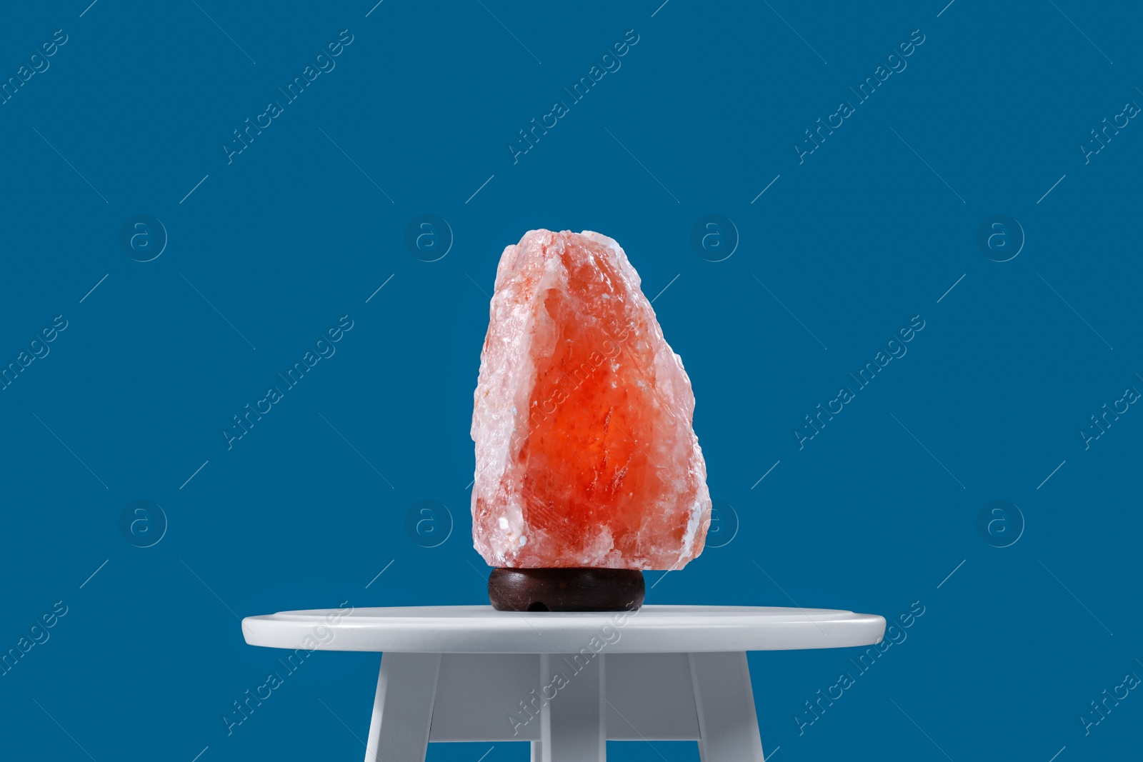 Photo of Himalayan salt lamp on white table against blue background