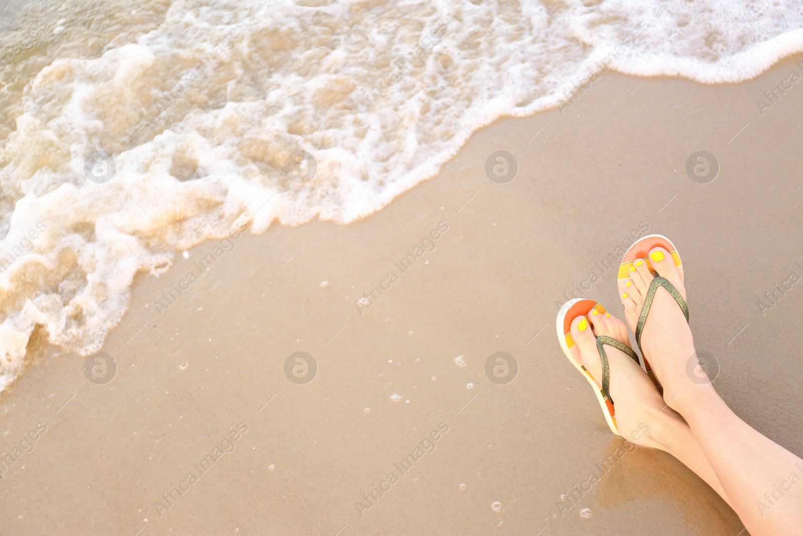 Photo of Closeup of woman with stylish flip flops on sand near sea, space for text. Beach accessories