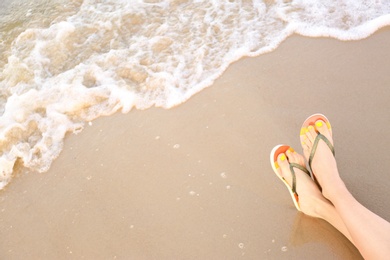 Photo of Closeup of woman with stylish flip flops on sand near sea, space for text. Beach accessories