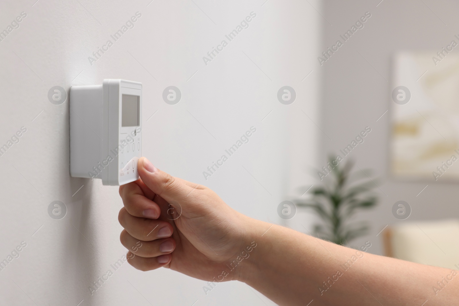 Photo of Woman adjusting thermostat on white wall indoors, closeup. Smart home system