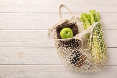 Net bag with different items on white wooden table, top view and space for text. Conscious consumption