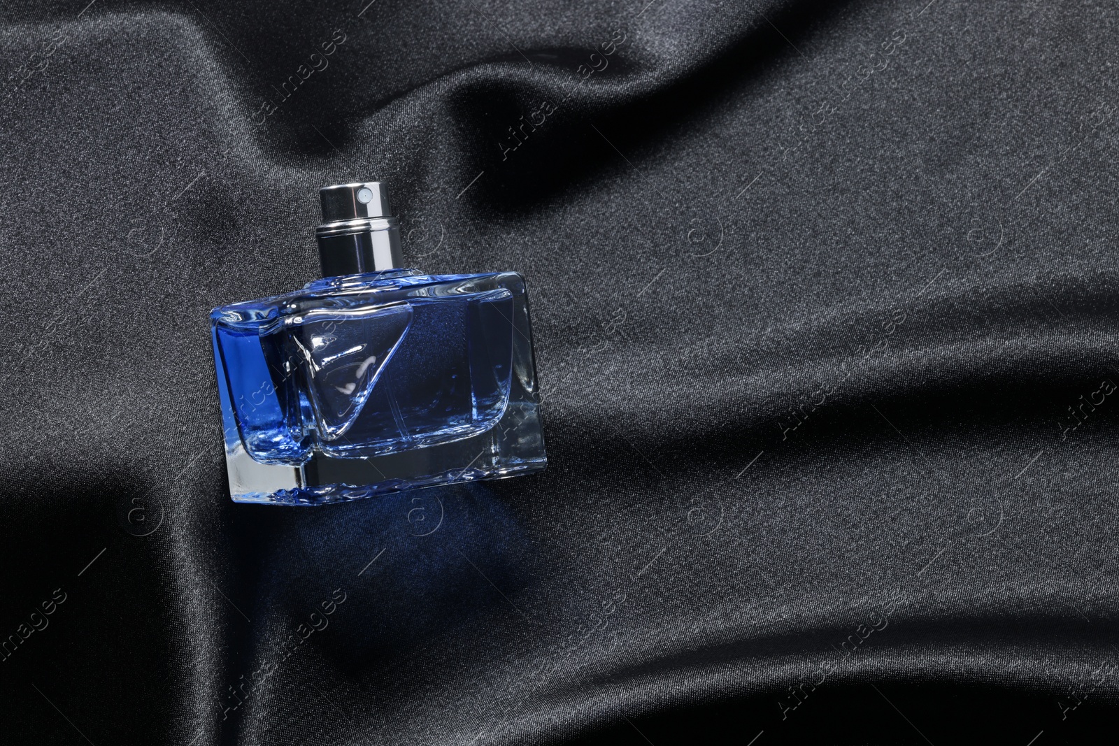 Photo of Luxury men's perfume in bottle on black satin fabric, top view. Space for text