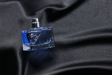 Luxury men's perfume in bottle on black satin fabric, top view. Space for text