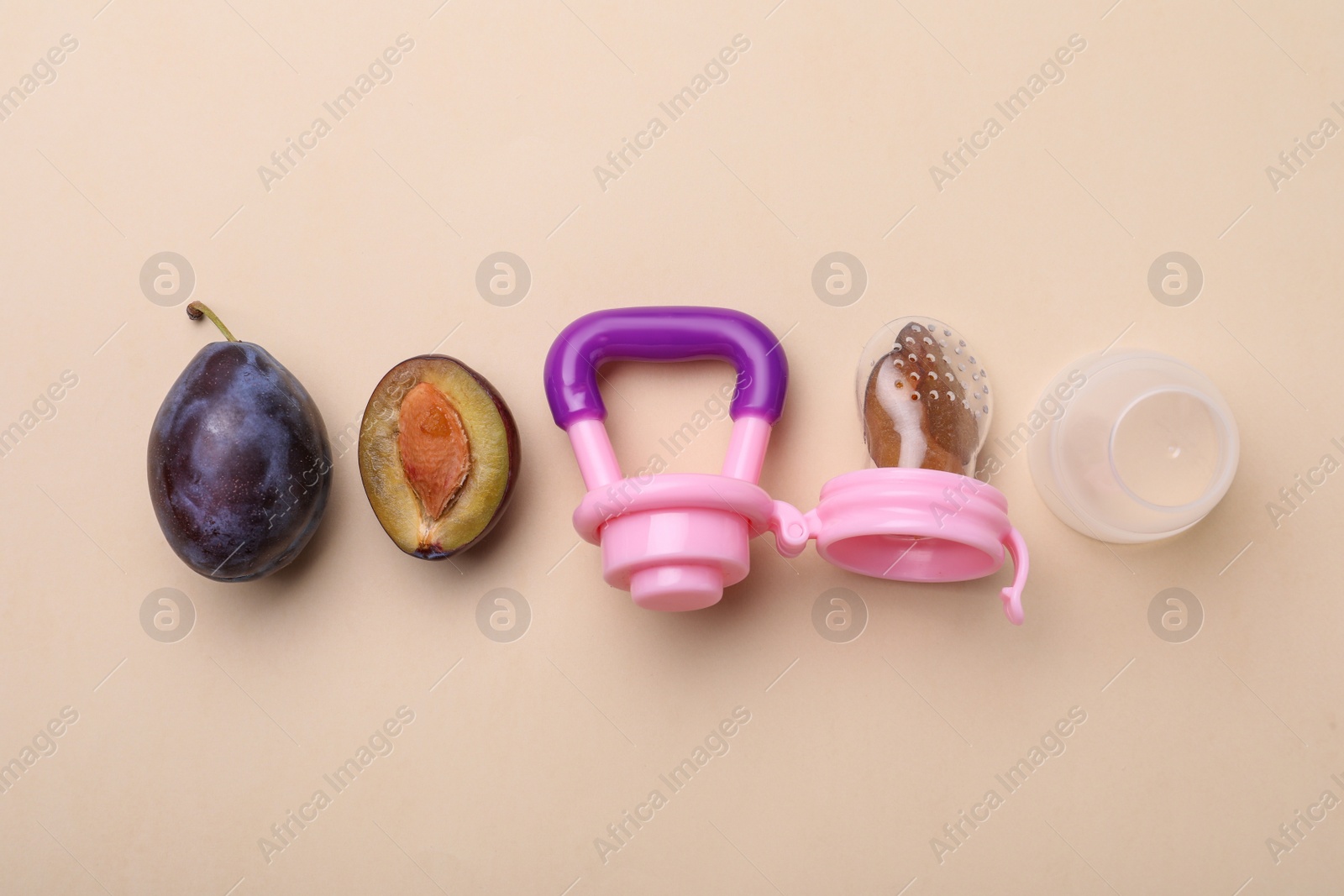 Photo of Nibbler with fresh plum on beige background, flat lay. Baby feeder