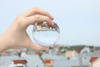 Photo of View of beautiful city street, overturned reflection. Man holding crystal ball outdoors, closeup