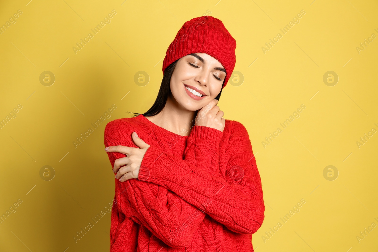 Photo of Young woman wearing warm sweater and hat on yellow background. Winter season