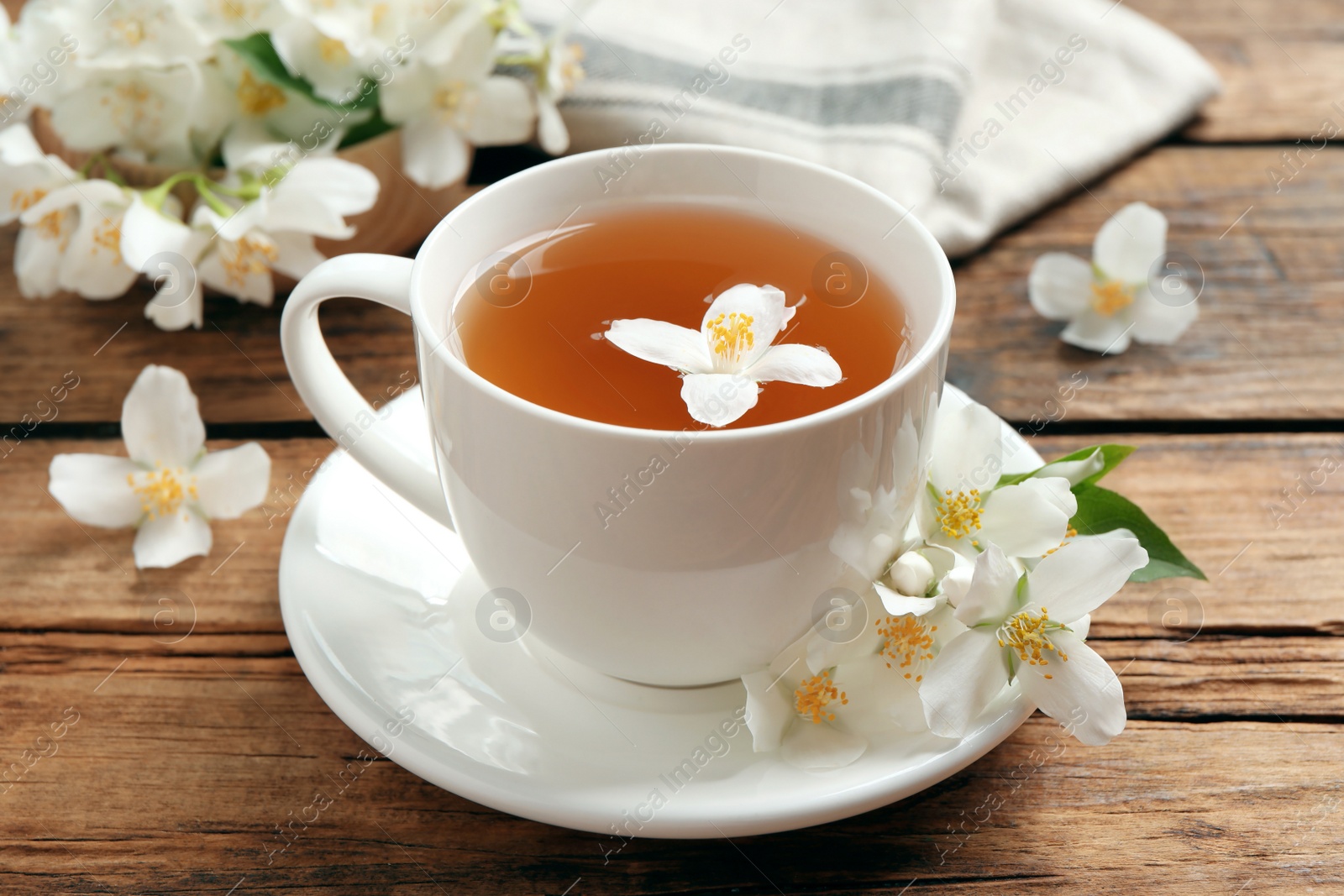 Photo of Cup of aromatic jasmine tea and fresh flowers on wooden table