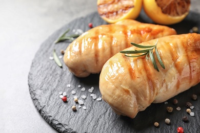 Slate plate with grilled chicken breasts and lemon on table, closeup