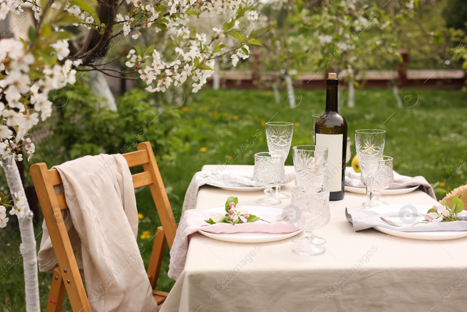 Photo of Stylish table setting with beautiful spring flowers, wine, plates and glasses in garden