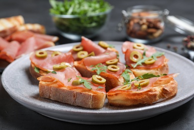 Delicious bruschettas with prosciutto and olives on table, closeup