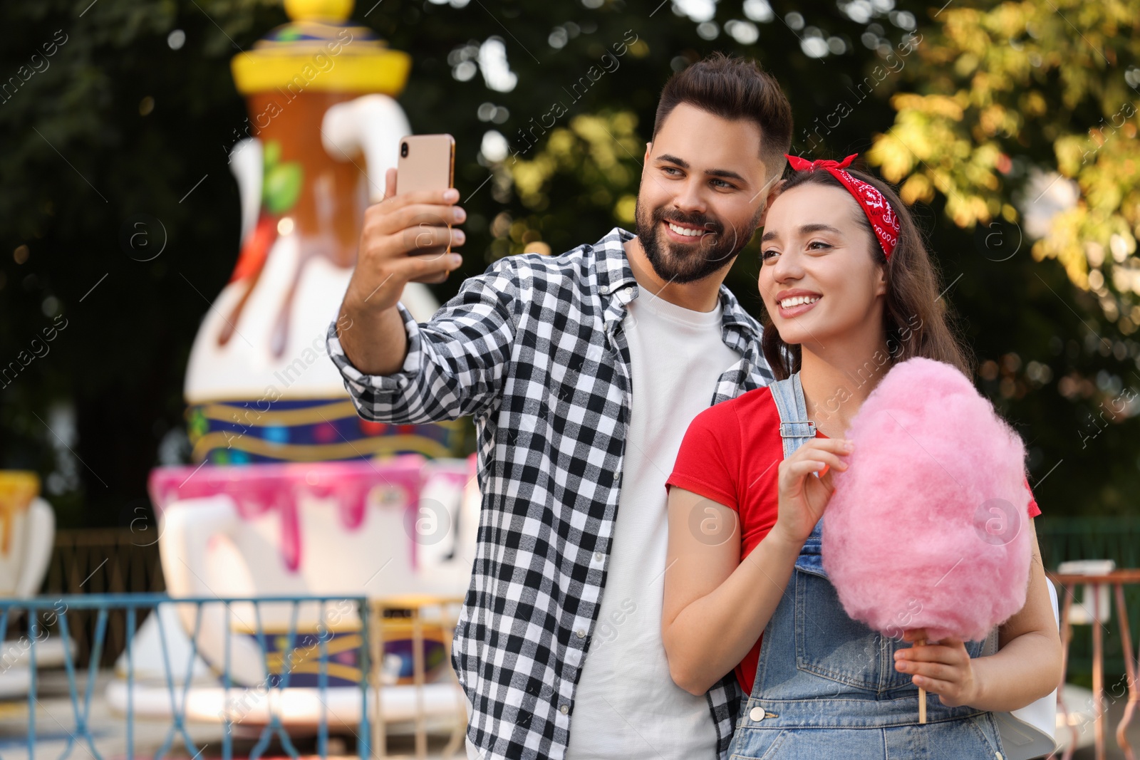 Photo of Happy young man and his girlfriend with cotton candy taking selfie at funfair