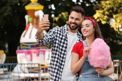 Photo of Happy young man and his girlfriend with cotton candy taking selfie at funfair