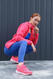 Beautiful woman in gym clothes posing near dark grey wall on street