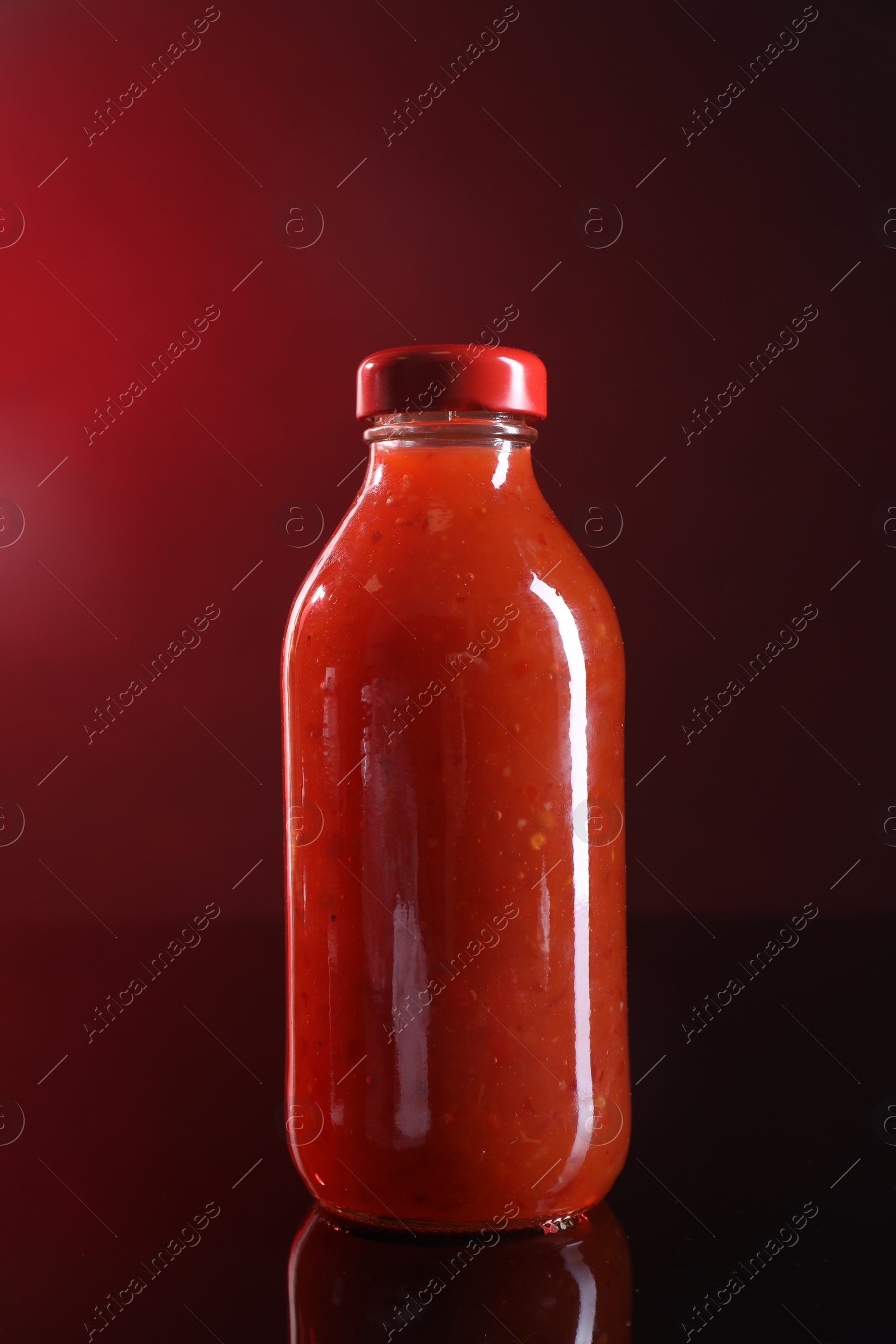 Photo of Spicy chili sauce in bottle on against dark background