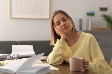 Young tired woman studying at wooden table in room