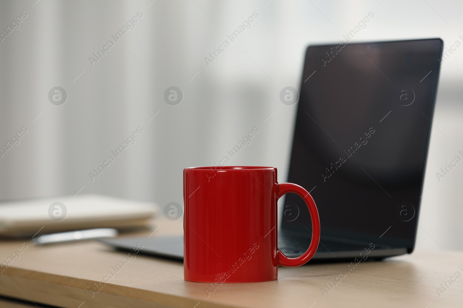 Photo of Red ceramic mug and laptop on wooden table at workplace