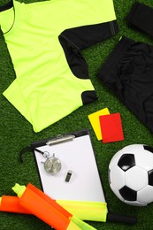Uniform, soccer ball and other referee equipment on green grass, flat lay