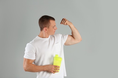 Photo of Athletic young man with protein shake on light grey background