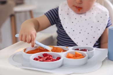 Photo of Little baby eating food in high chair at kitchen, closeup