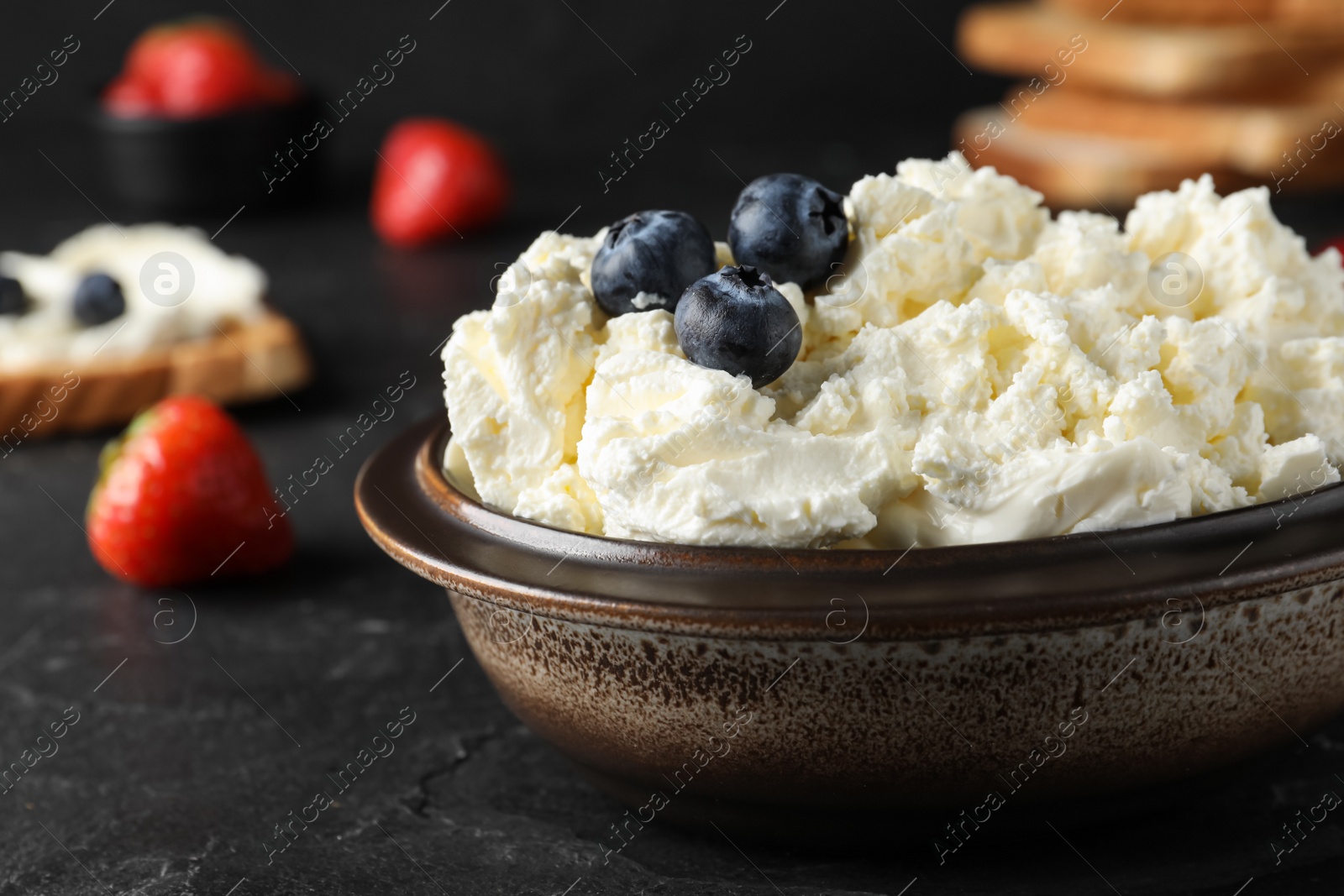Photo of Tasty cream cheese and fresh berries on black table