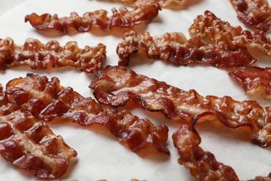 Photo of Slices of tasty fried bacon on white table, closeup