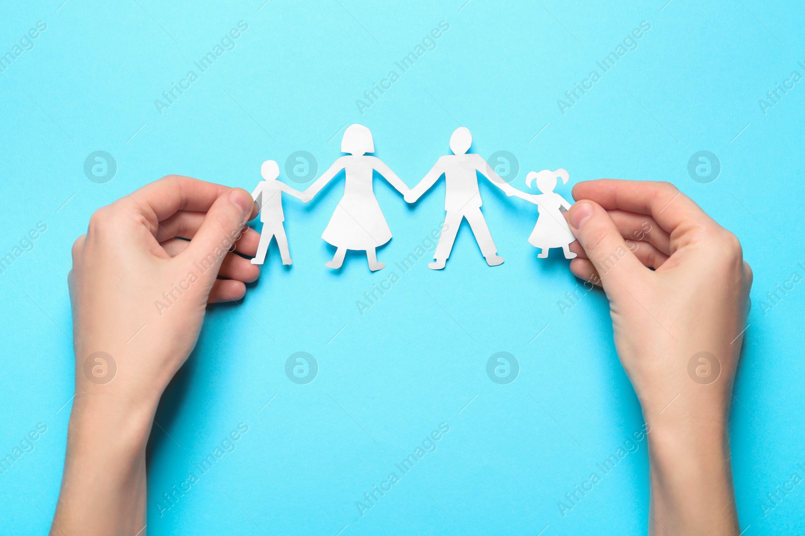 Photo of Woman holding paper cutout of family on light blue background, top view