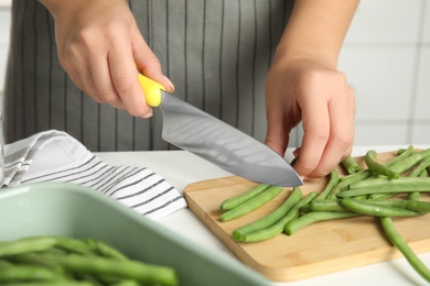 Photo of Woman cutting green beans at white table, closeup