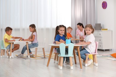 Photo of Group of cute little children and nursery teacher drawing at desks in kindergarten. Playtime activities
