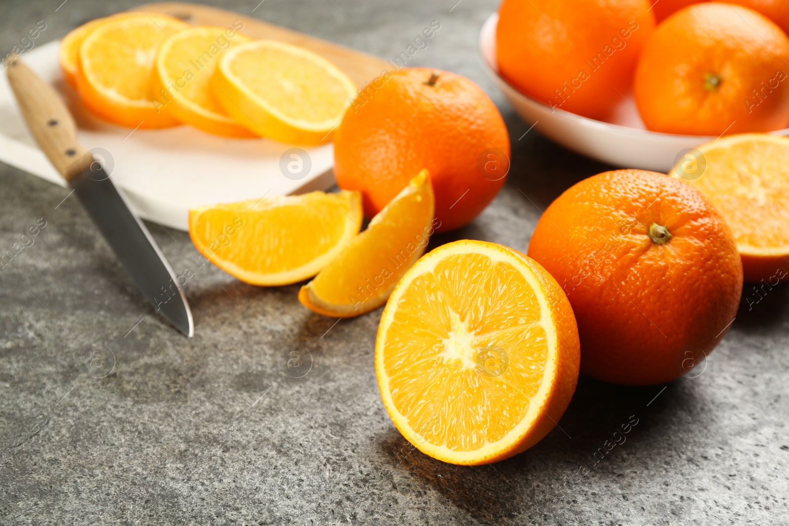 Photo of Whole and cut delicious ripe oranges on grey table