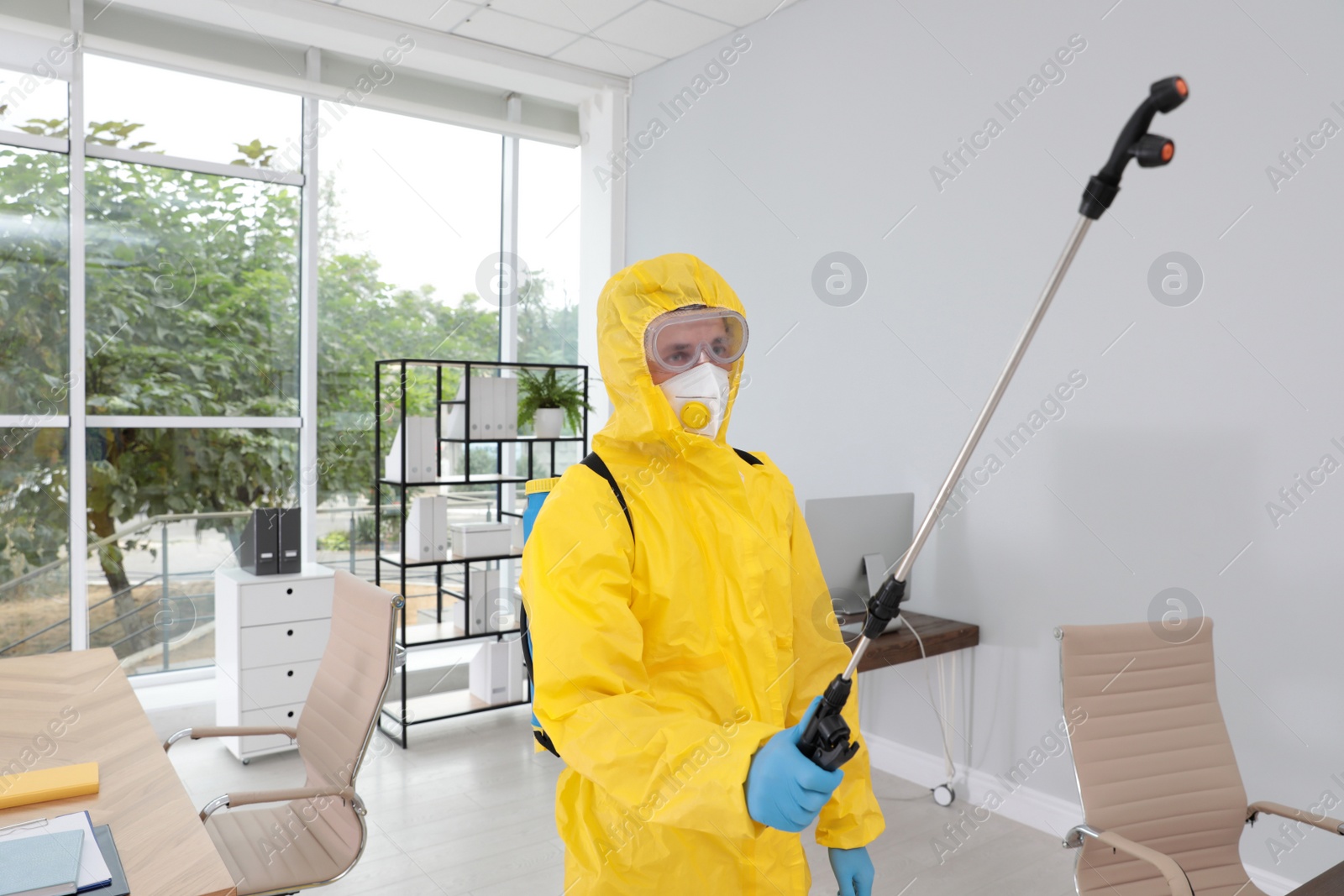 Photo of Janitor in protective suit disinfecting office to prevent spreading of COVID-19