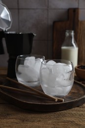 Photo of Making iced coffee. Ice cubes in glasses and straws on wooden table