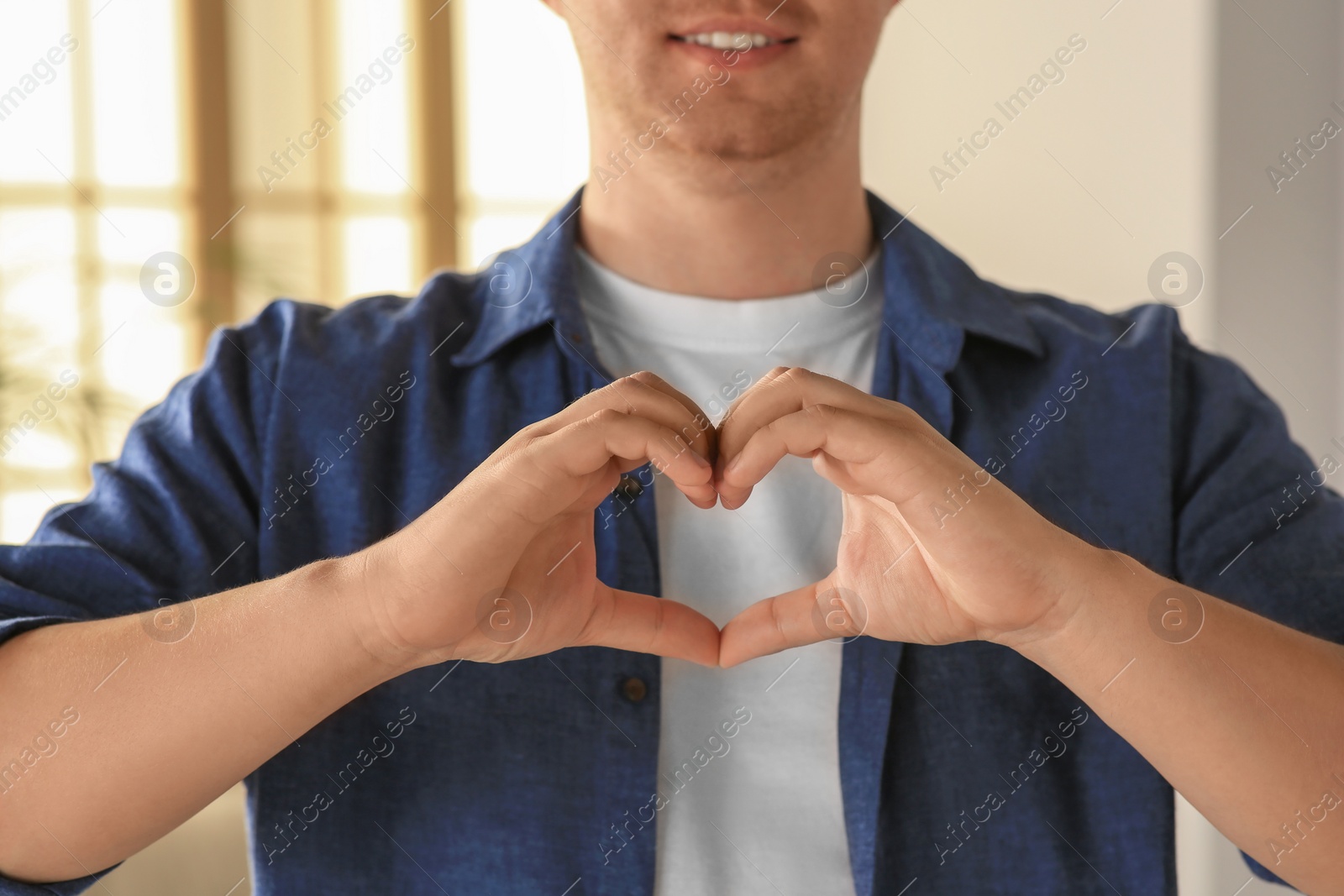 Photo of Man making heart with hands indoors, closeup. Volunteer concept