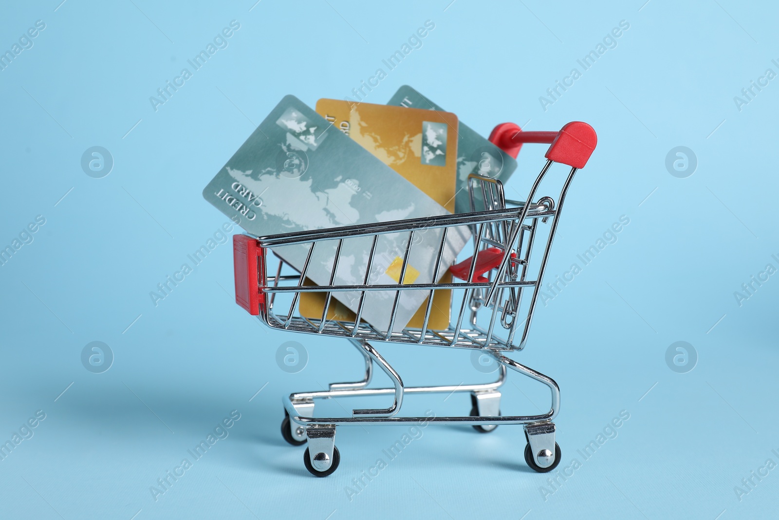 Photo of Small metal shopping cart with credit cards on light blue background