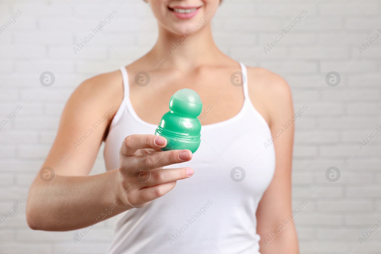 Photo of Young woman holding roll-on deodorant against brick wall, closeup