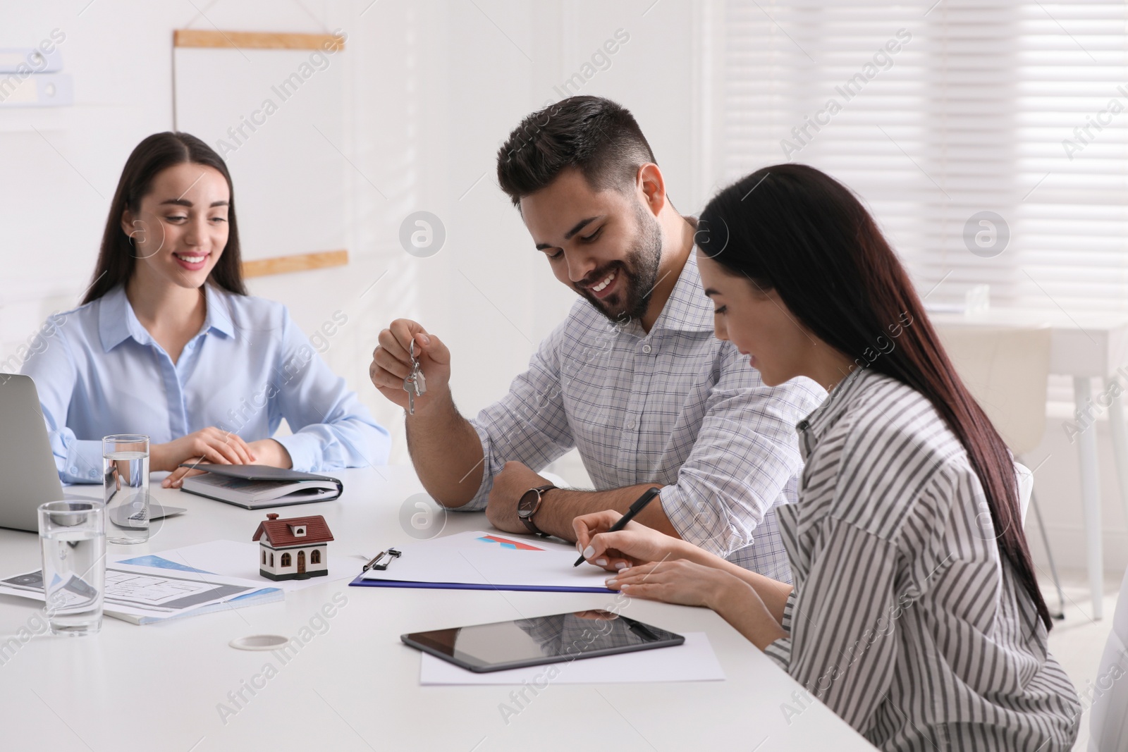 Photo of Happy young couple signing purchase contract in real estate agent's office. Mortgage concept