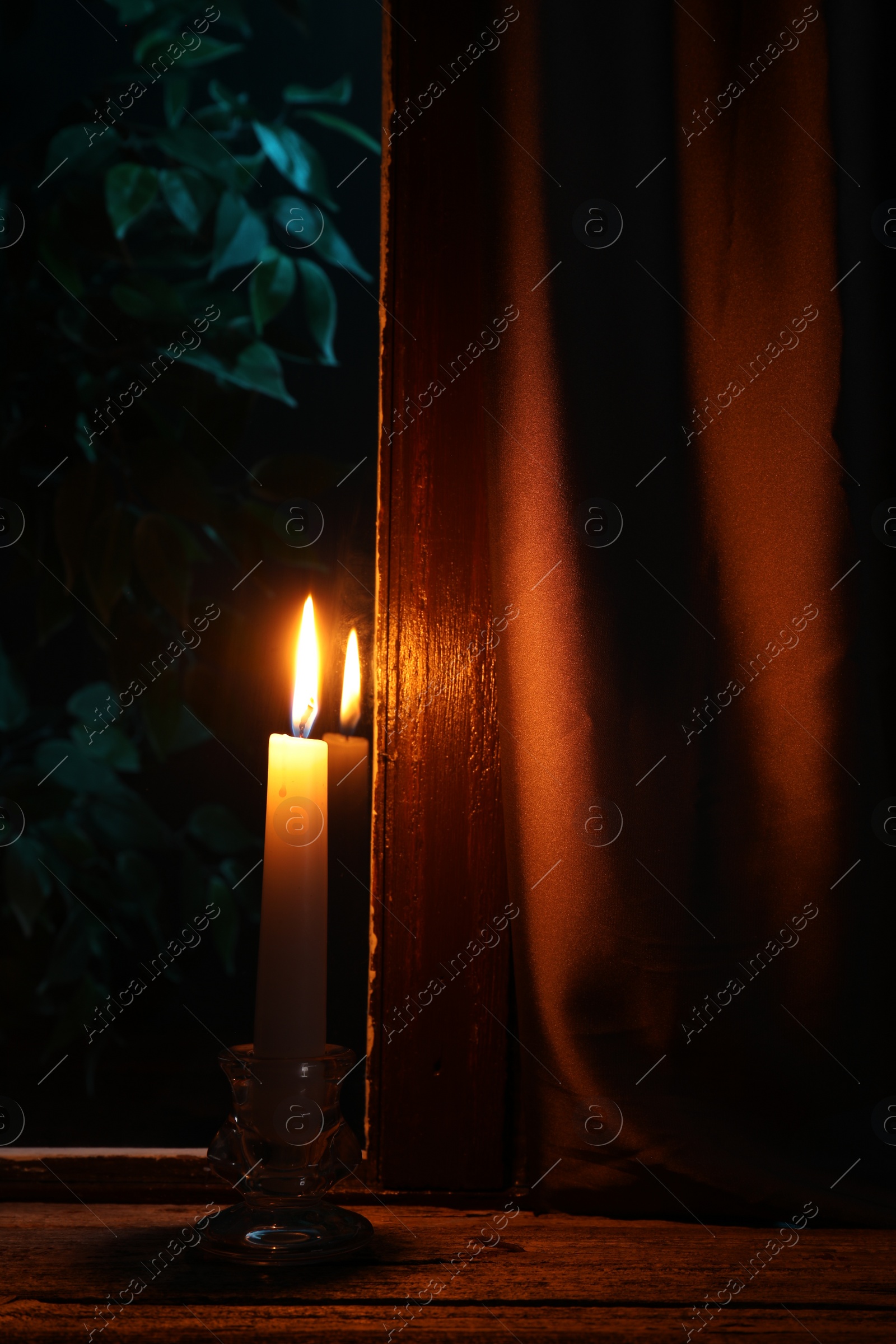 Photo of Burning candle on wooden table near window at night